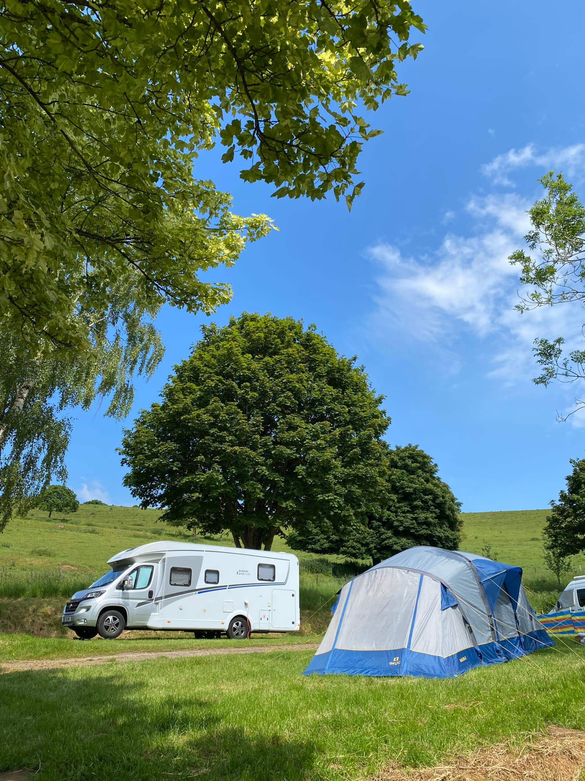 Motorhome and tent pitched on a sunny day at Batcombe Vale Campsite near mature trees